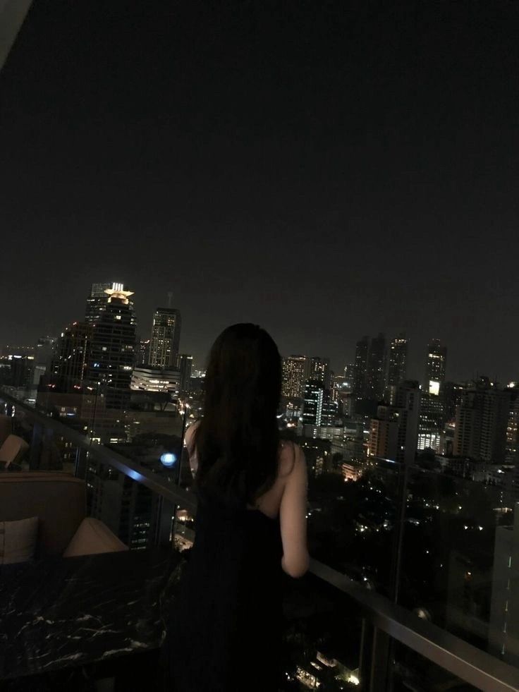 Gái trẻ trong váy đen ngắm phố đêm lãng mạn từ ban công