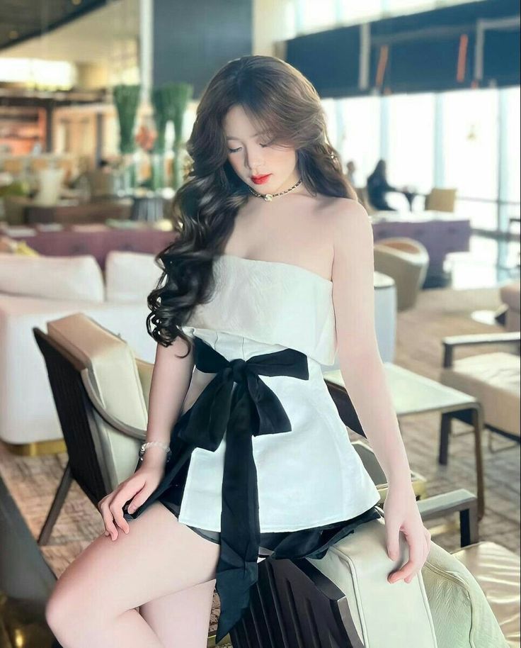 Gái xinh mặc áo quây trắng kết hợp với váy đen, tạo dáng ngồi trong quán cà phê