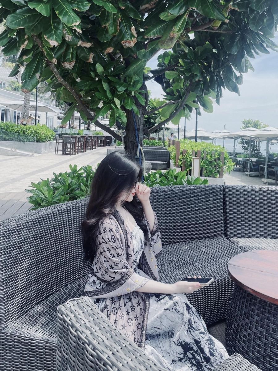 Gái xinh mặc đầm hoa và áo khoác mỏng ngồi trên sofa nhựa