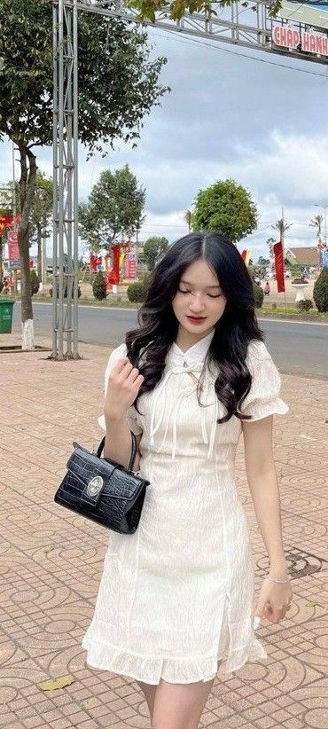Gái xinh mặc đầm trắng cầm túi xách nhỏ đi bộ trên vỉa hè