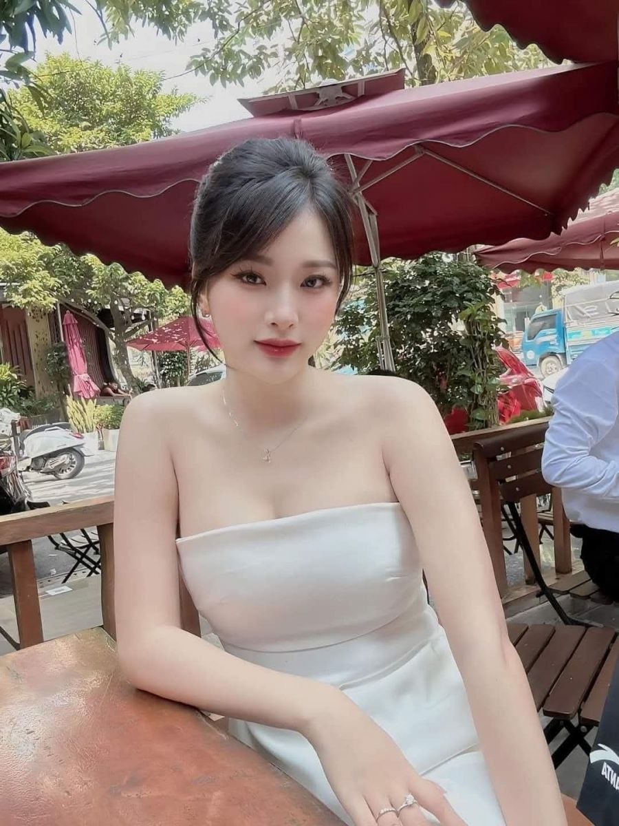 Gái xinh mặc váy trắng ngồi thư giãn tại quán cà phê ngoài trời