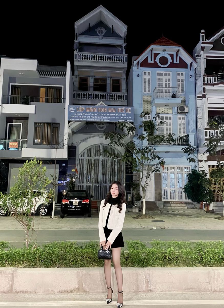 Gái xinh mặc váy trắng và áo khoác đen bên ngôi nhà lớn