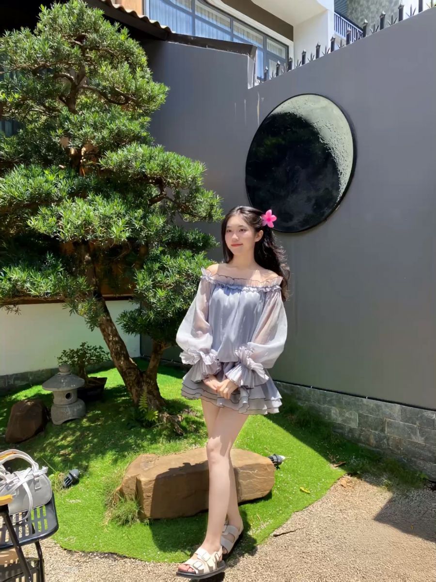 Gái xinh mặc váy xếp ly màu xám bên cây bonsai
