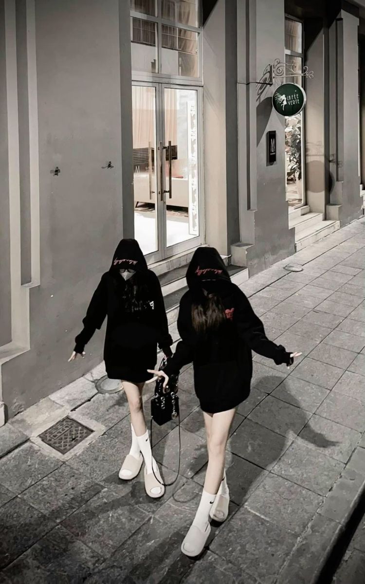 Hai cô gái mặc áo hoodie đen đi bộ trên phố vào buổi tối