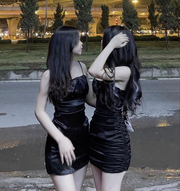 Hai cô gái mặc đầm đen ôm sát đứng cạnh nhau trong phố đêm