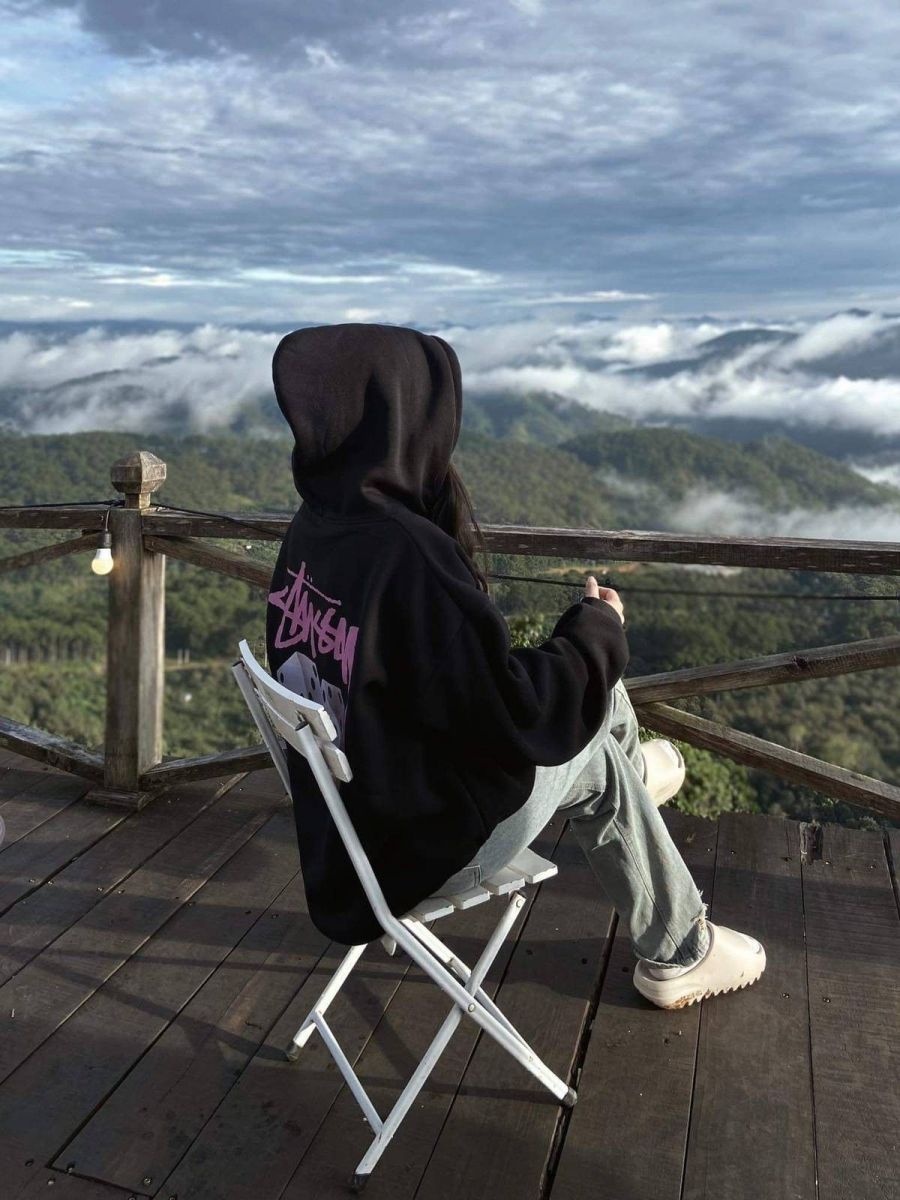 Ảnh cô gái mặc hoodie đen ngồi trên ghế nhìn ra núi và biển