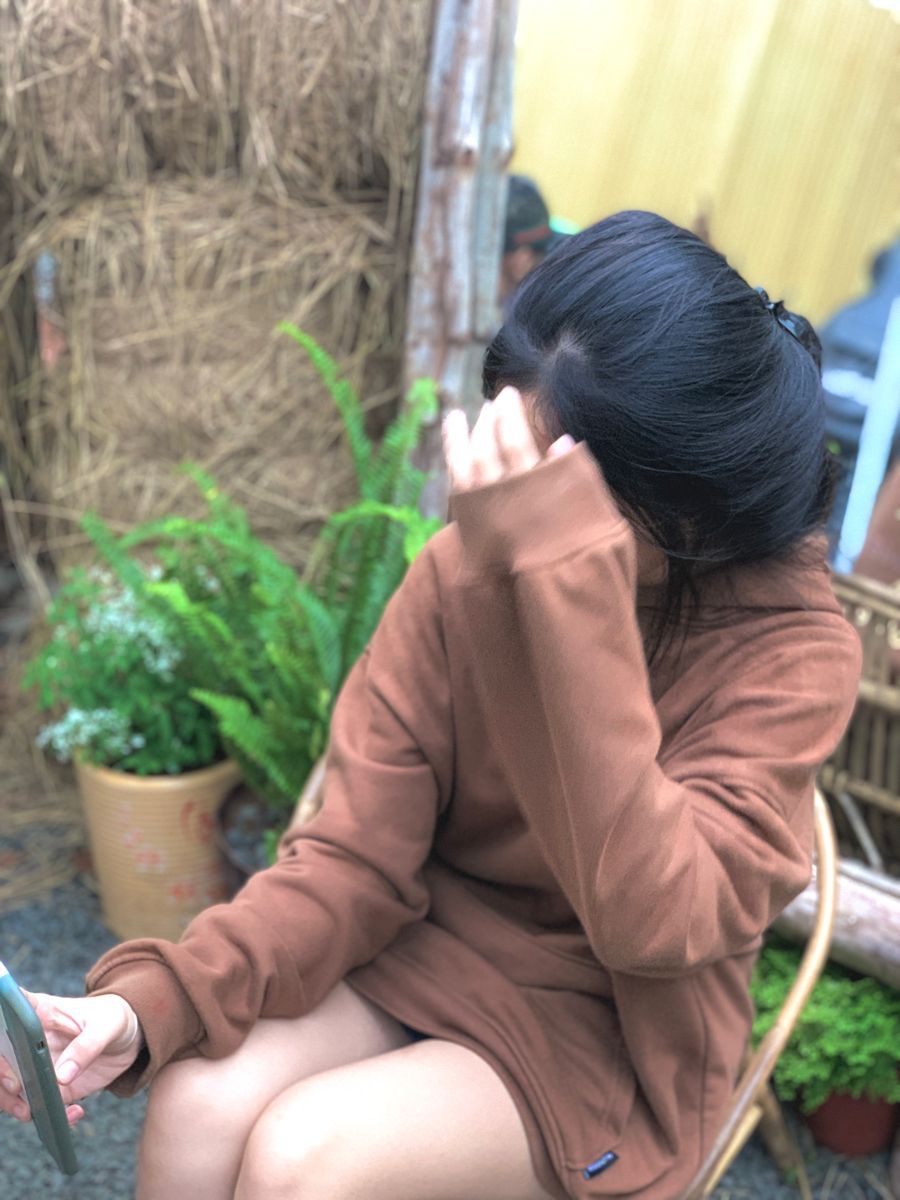 Ảnh cô gái trẻ mặc áo hoodie nâu ngồi trên ghế sử dụng điện thoại