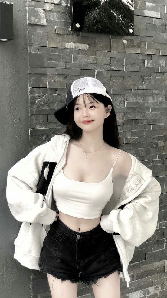 Ảnh gái trẻ mặc áo crop top trắng và quần short đen bên tường đá