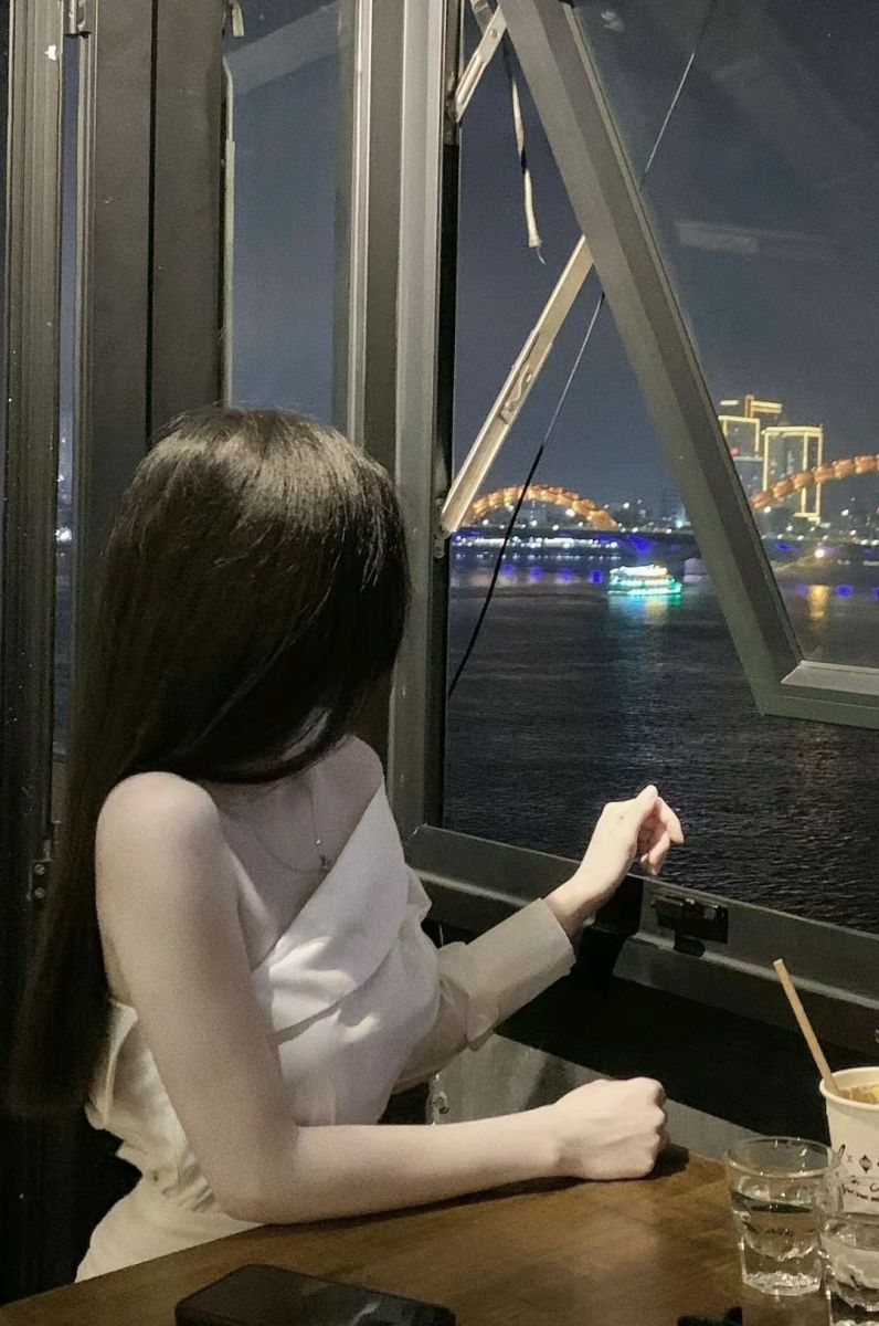 Ảnh gái trẻ mặc áo hai dây trắng ngồi bên cửa sổ quán cà phê