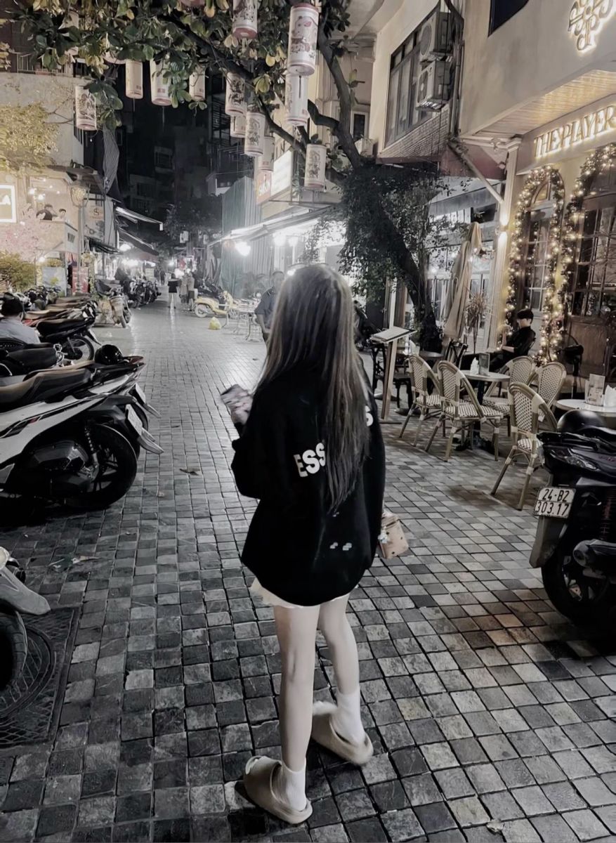 Ảnh gái trẻ mặc áo hoodie đen và quần ngắn đi bộ trên phố đêm