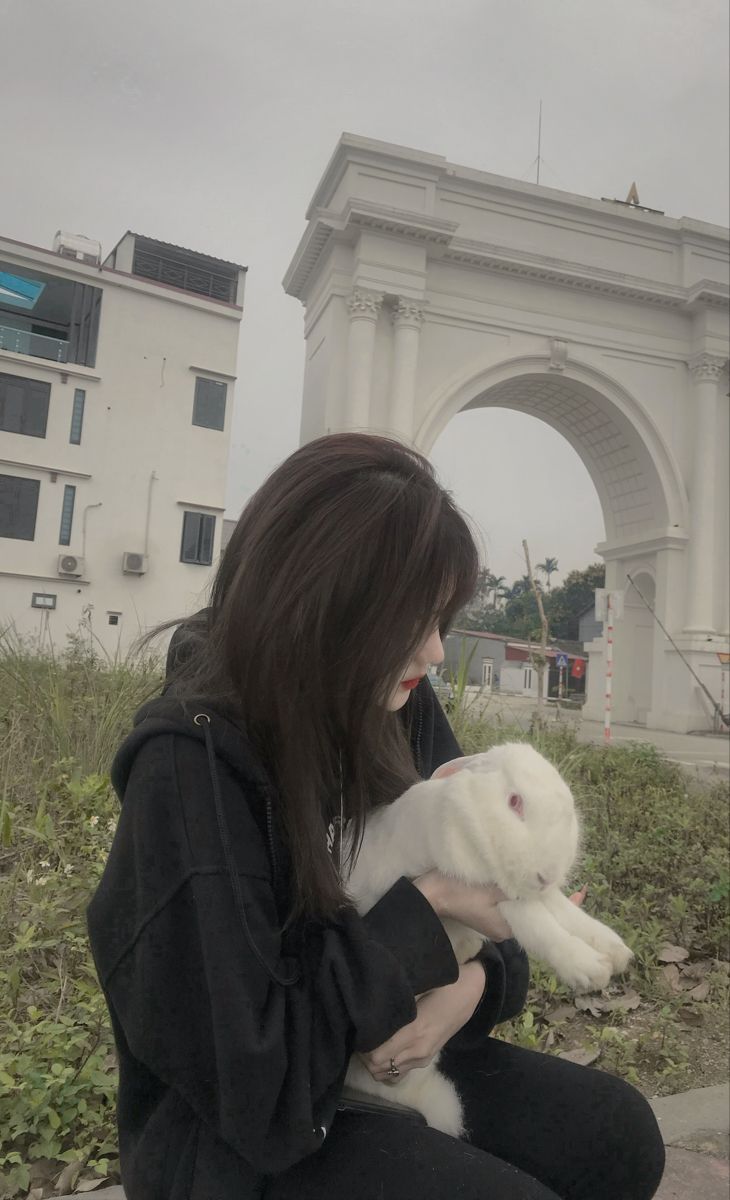 Ảnh gái trẻ mặc áo hoodie đen và quần tối ôm một con thỏ trắng