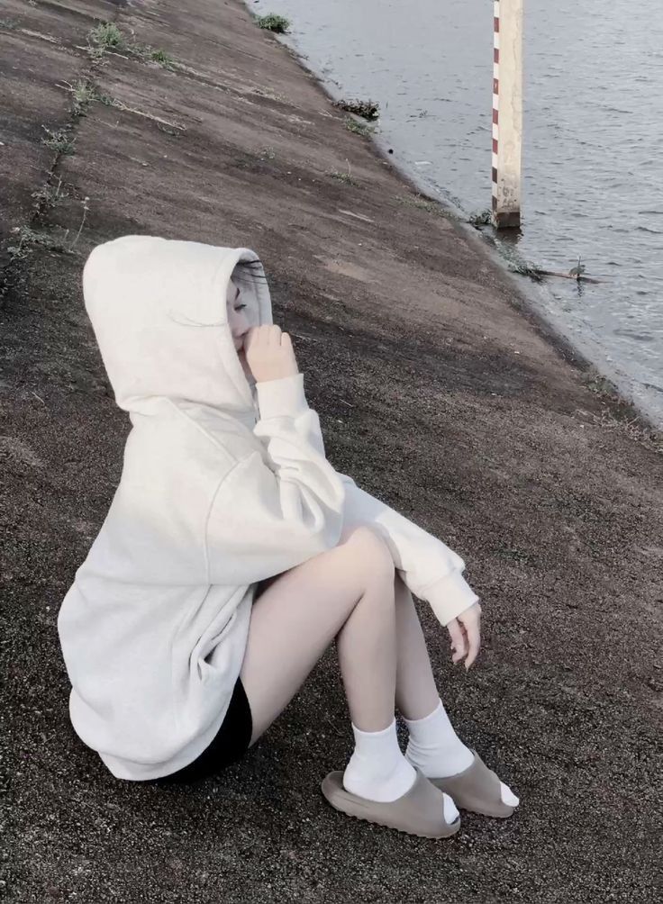 Ảnh gái trẻ mặc áo hoodie trắng và quần shorts đen bên bờ nước