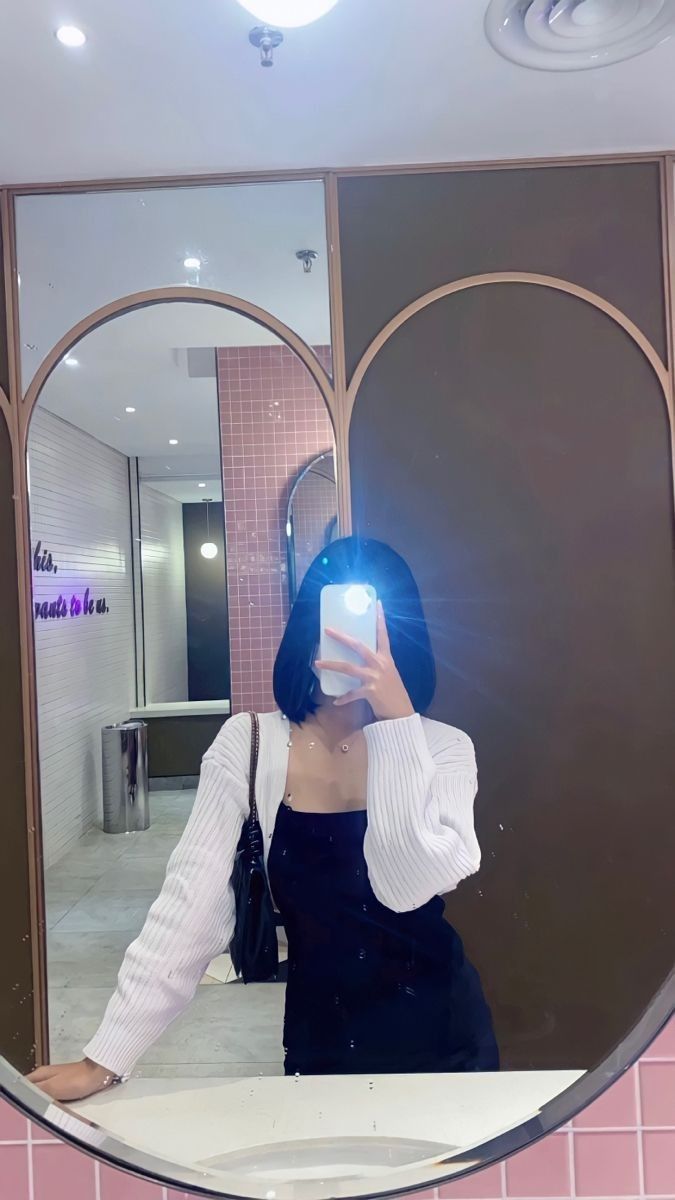 Ảnh gái trẻ mặc áo khoác cardigan trắng và váy đen chụp selfie trong gương