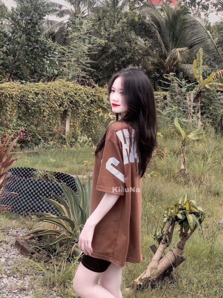 Ảnh gái trẻ mặc áo phông nâu và quần đùi đen giữa vườn cây xanh