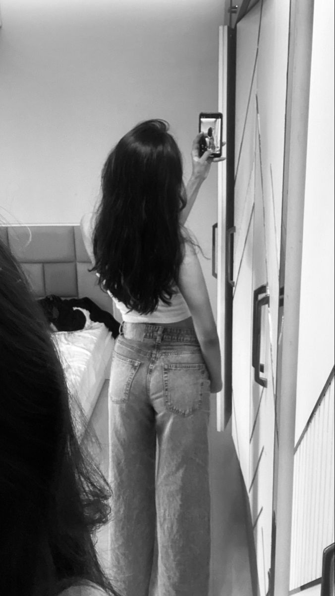 Ảnh gái trẻ mặc áo trắng và quần jeans rộng chụp selfie trong phòng ngủ