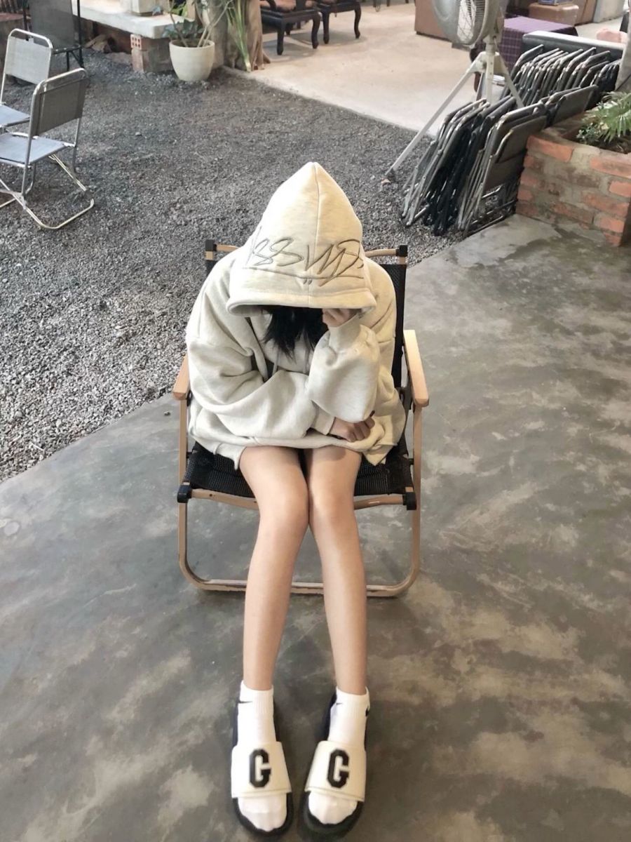 Ảnh gái trẻ mặc hoodie xám ngồi ghế xếp trong không gian nội thất thoáng đãng