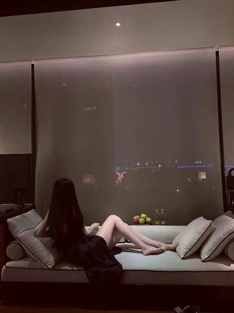 Ảnh gái trẻ mặc váy đen ngồi trên ghế sofa ngắm cảnh thành phố
