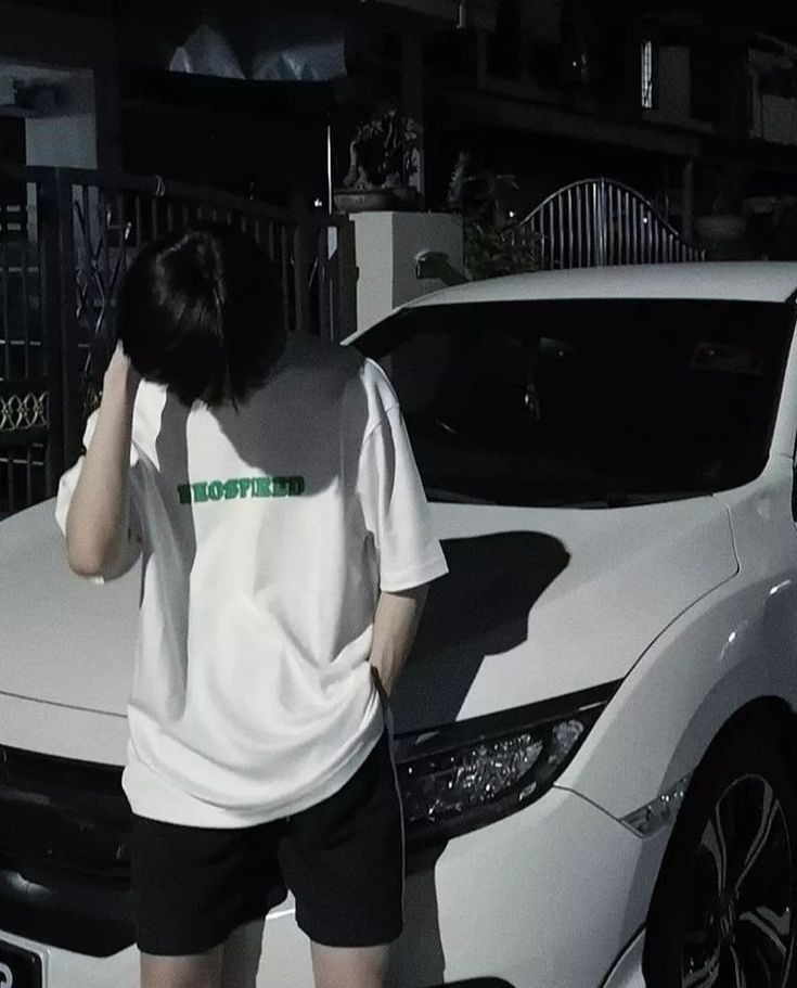 Anh nam giới mặc áo phông trắng và quần short đen bên xe ô tô