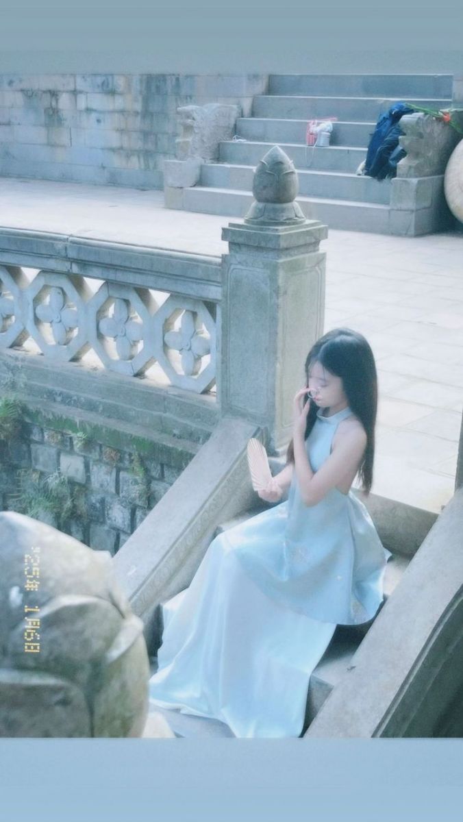 Cô gái đẹp mặc váy xanh ngồi trên bậc thang đá cam quýt