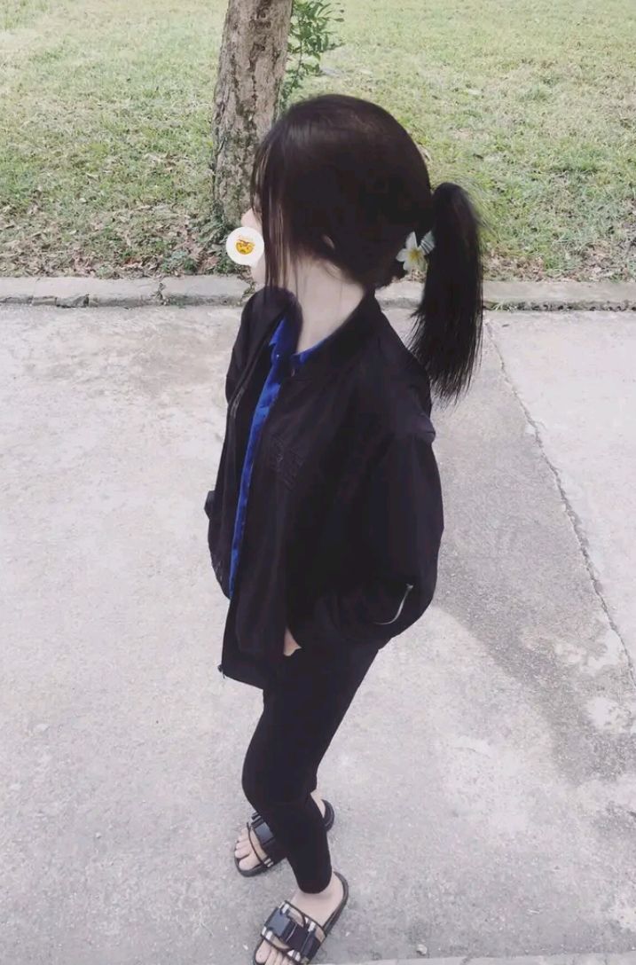 Cô gái đẹp trong áo khoác đen và quần legging, tạo dáng bên gốc cây
