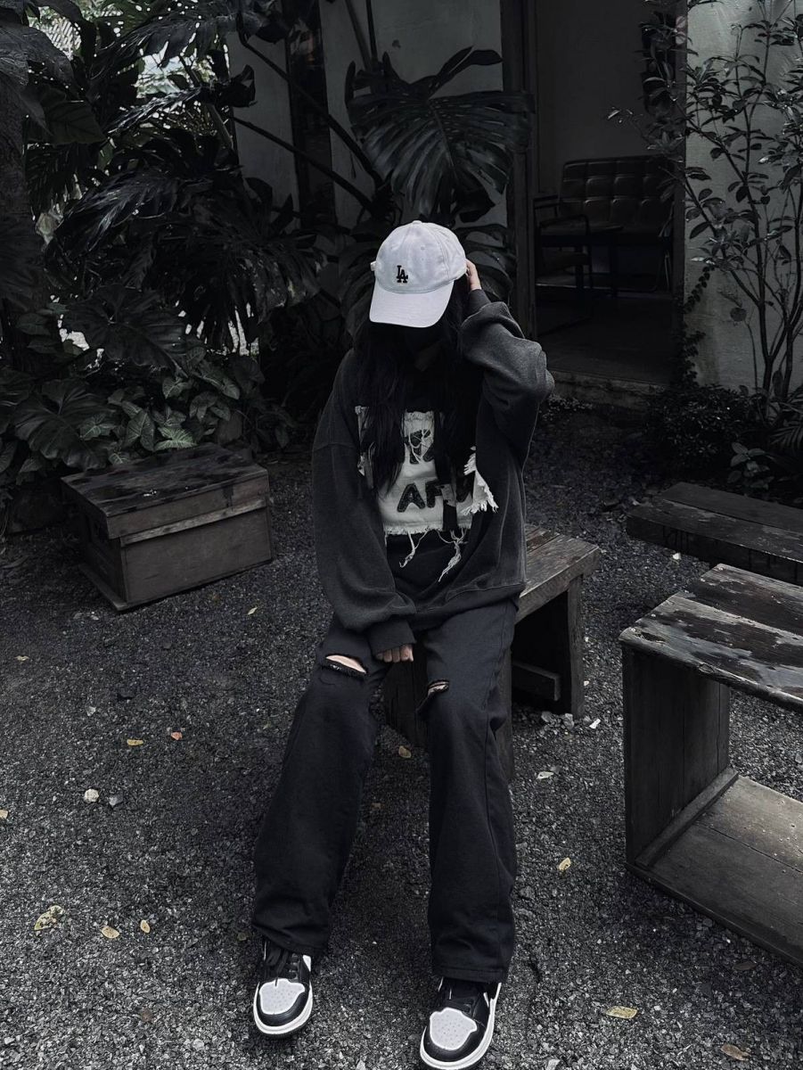 Cô gái mặc áo hoodie đen và quần jeans rách ngồi trong vườn