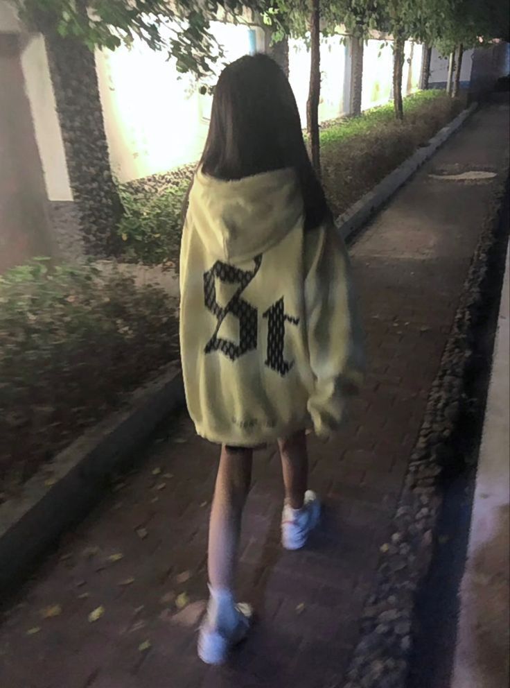 Cô gái mặc áo hoodie vàng đi bộ trên vỉa hè đêm