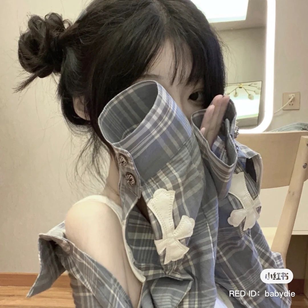 Cô gái trẻ diện áo sơ mi caro rỗng ngồi tạo dáng trong phòng ngủ ấm cúng