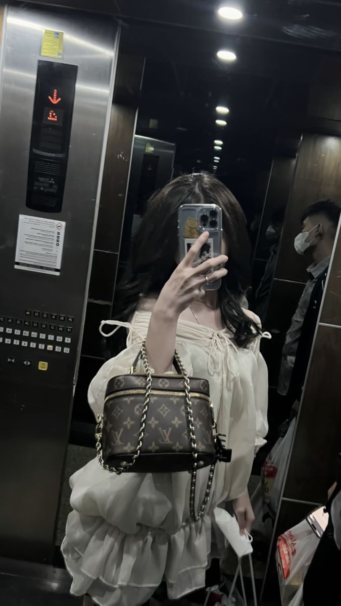 Cô gái trẻ mặc áo blouse trắng nhẹ nhàng, cầm túi xách Louis Vuitton