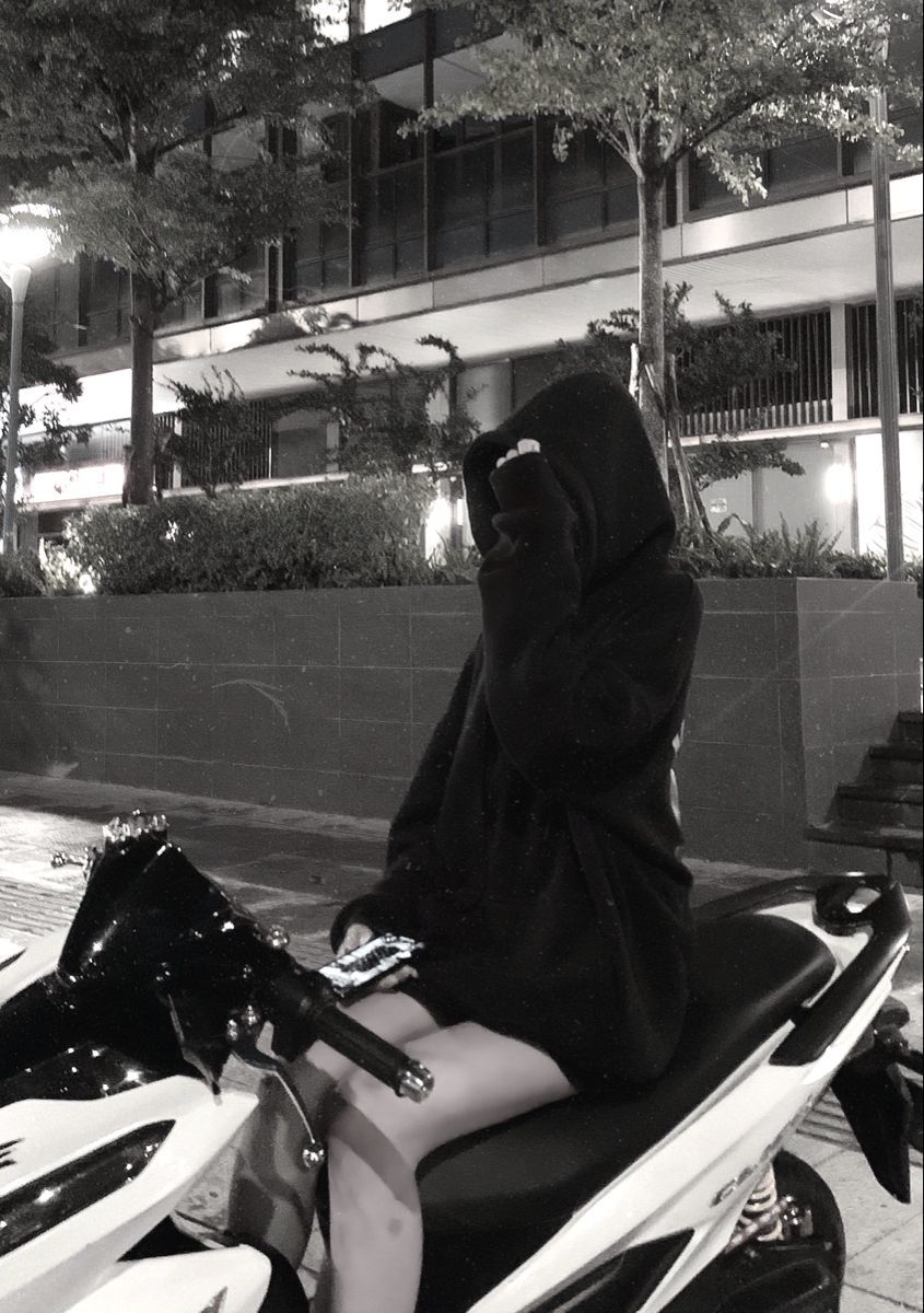 Cô gái trẻ mặc áo hoodie đen ngồi trên xe máy