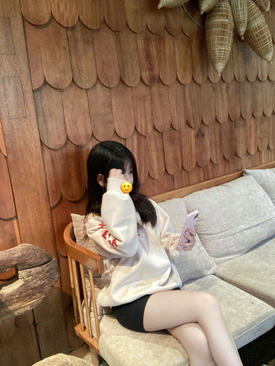 Cô gái trẻ mặc áo hoodie trắng và quần shorts đen ngồi trên ghế sofa