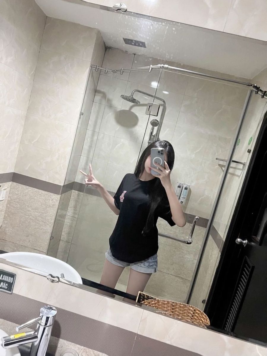 Cô gái trẻ mặc áo phông đen và quần shorts sáng màu chụp selfie