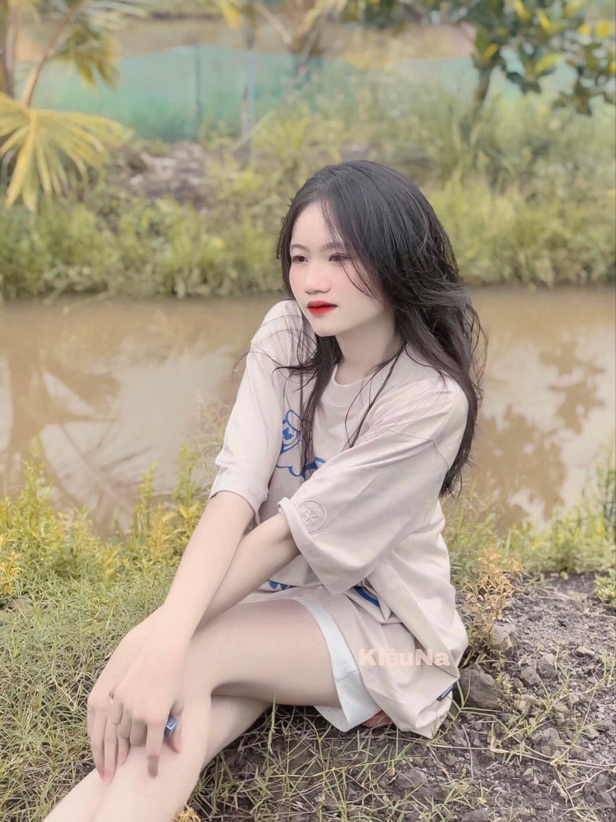 Cô gái trẻ mặc áo phông rộng và quần short ngồi bên bờ biển