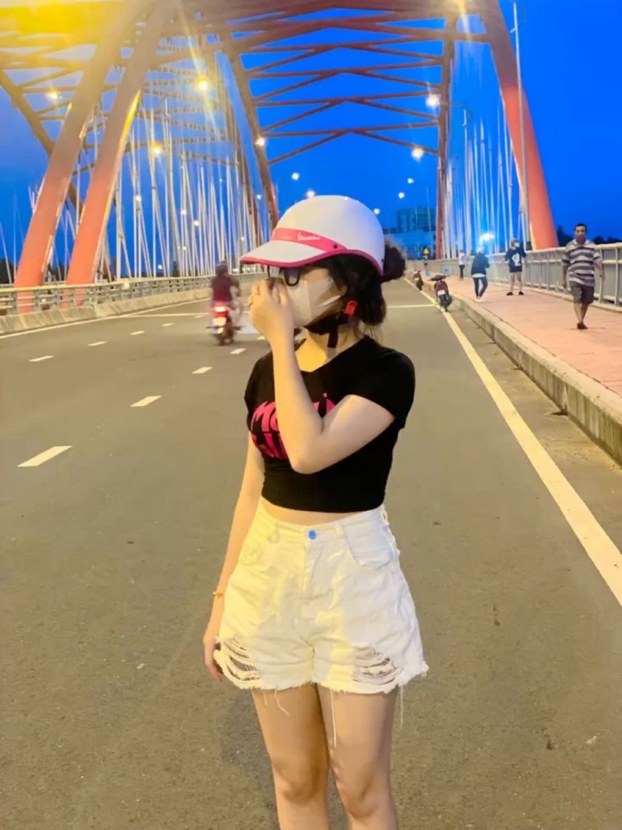 Cô gái trẻ mặc áo thun đen và quần short trắng trên cầu vào buổi tối