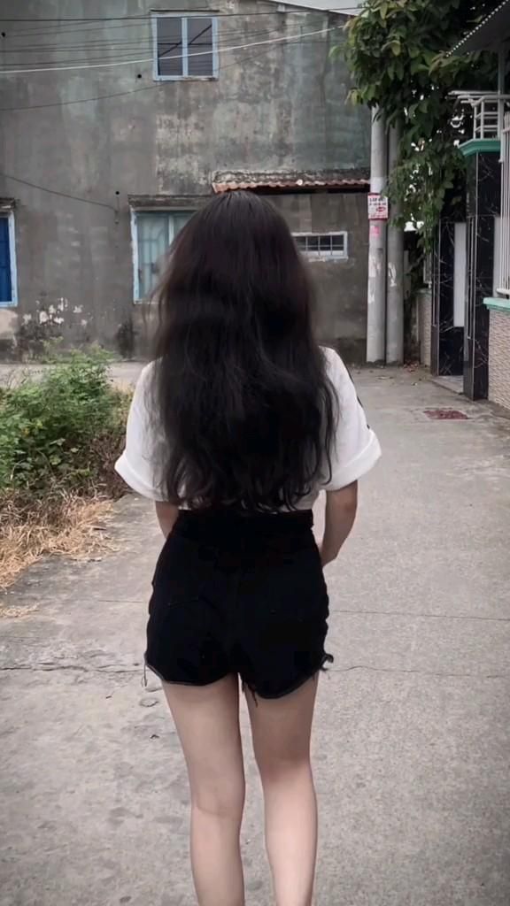 Cô gái trẻ mặc áo trắng và quần short đen đi bộ giữa phố cổ