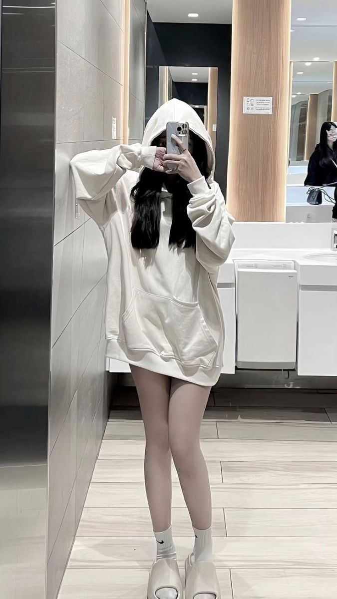 Cô gái trẻ mặc hoodie trắng trong nhà vệ sinh tự chụp ảnh selfie
