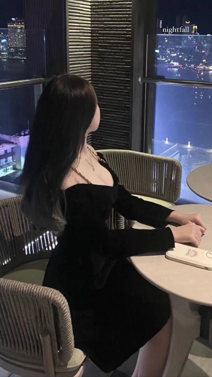 Cô gái trẻ mặc váy đen ngồi nghiêng tại quán cà phê
