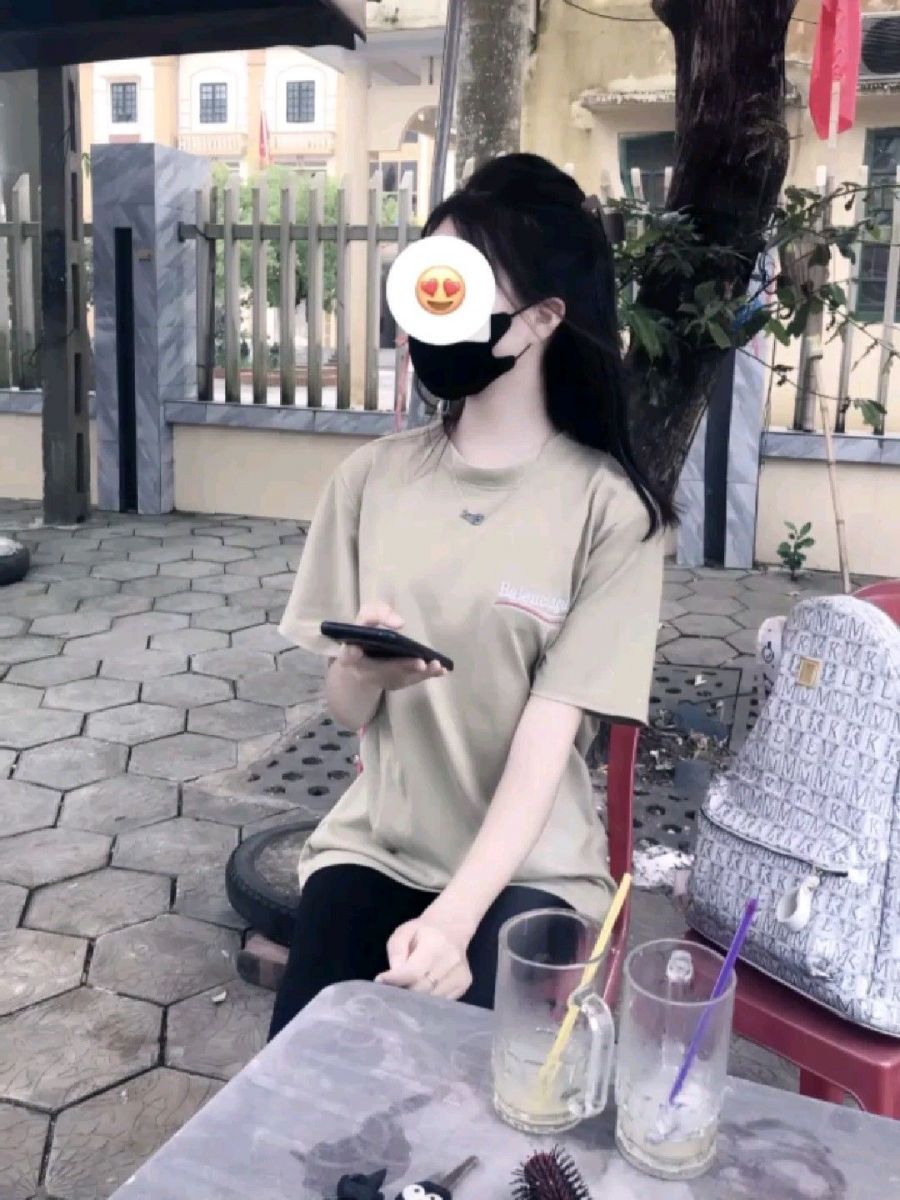 Cô gái trẻ xinh đẹp mặc áo phông màu be ngồi tại quán cà phê ngoài trời