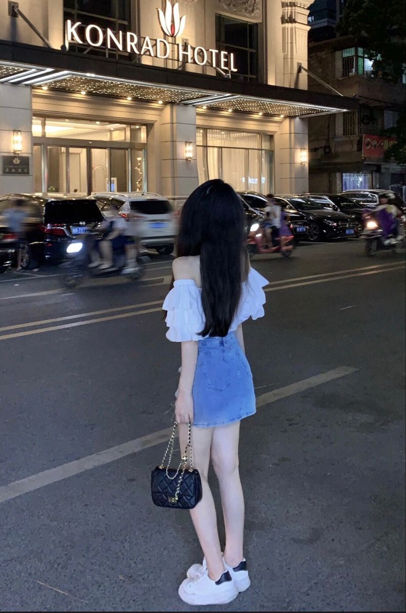 Cô gái trẻ xinh đẹp trong áo off-shoulder trắng và chân váy denim