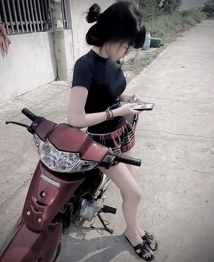 Cô gái xinh đẹp trong áo phông đen và chân váy kẻ caro bên chiếc xe máy đỏ