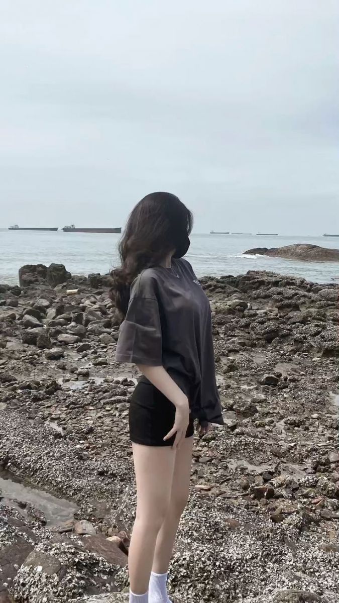 Cô gái xinh đẹp trong áo thun rộng và quần short đen bên bờ biển