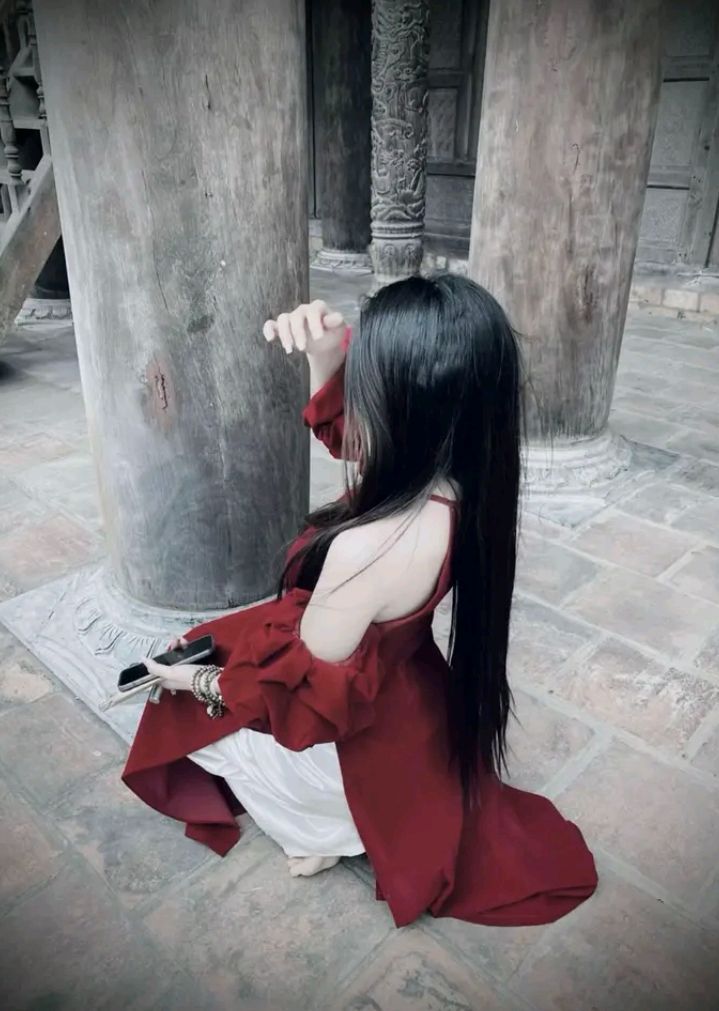 Cô gái xinh đẹp trong tà áo dài đỏ bên cột gỗ cổ