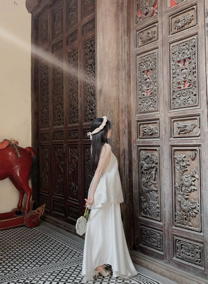 Cô gái xinh đẹp trong váy trắng bên bức tường gỗ chạm khắc