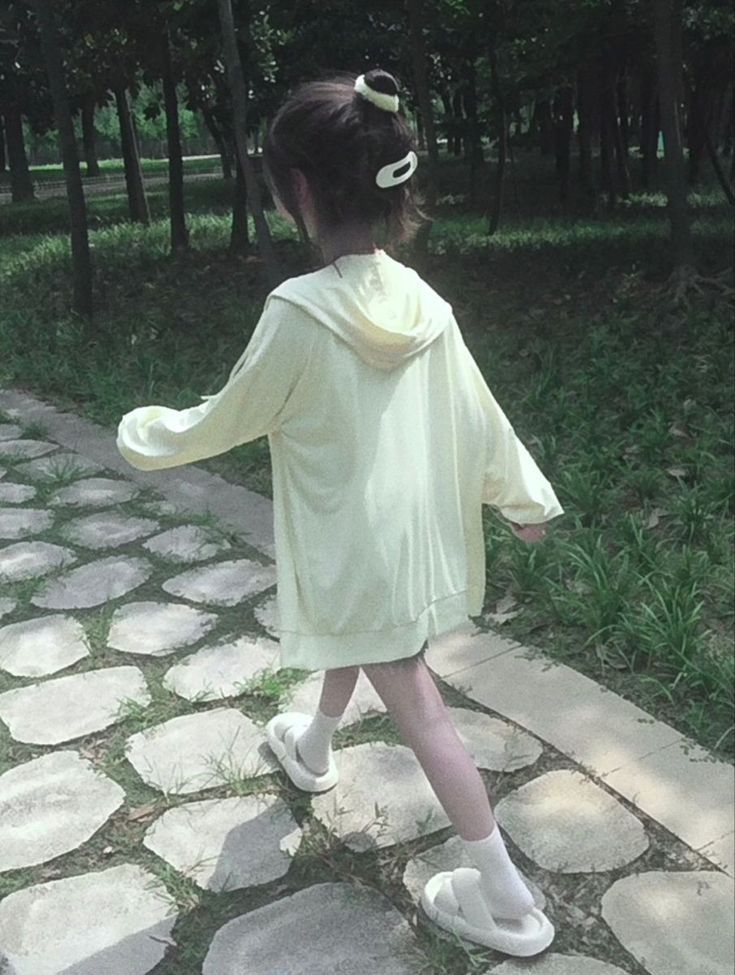 Cô gái xinh mặc áo hoodie vàng đi dạo trong công viên nhiều cây cối