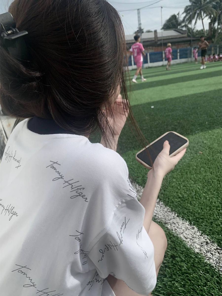 Cô gái xinh mặc áo phông trắng ngồi trên sân cỏ