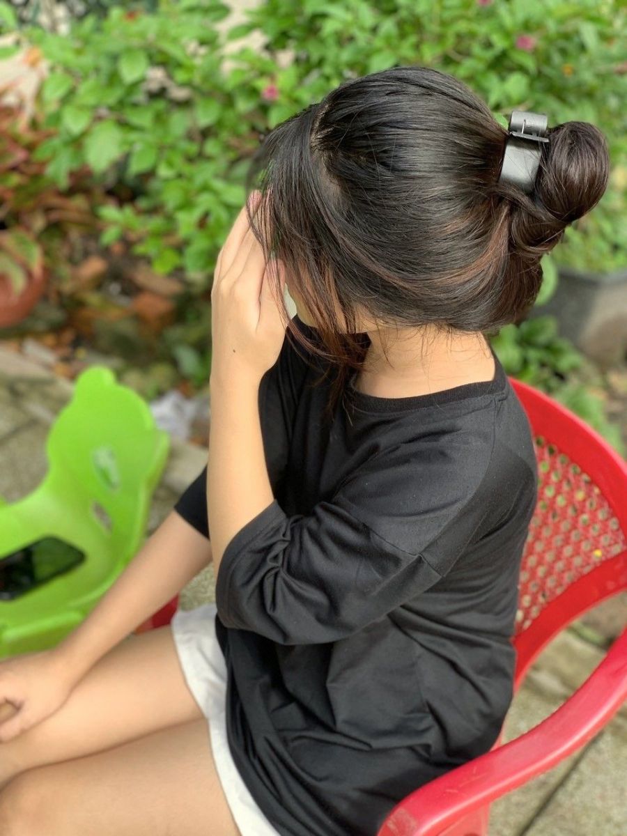 Gái che mặt ngồi trên ghế nhựa đỏ, mặc áo phông đen