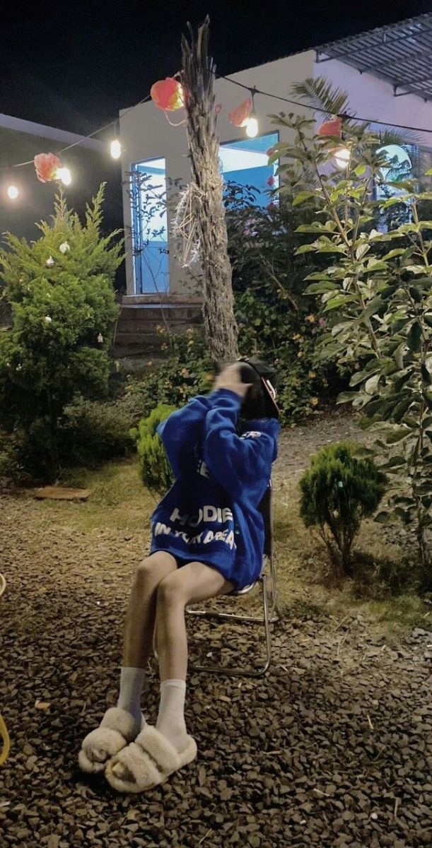 Gái che mặt trong áo hoodie xanh ngồi trên ghế giữa cây cối