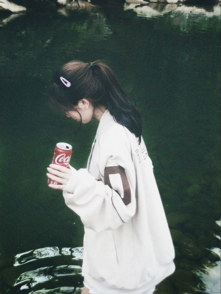 Gái trẻ diện áo khoác oversized Coca-Cola bên bờ nước