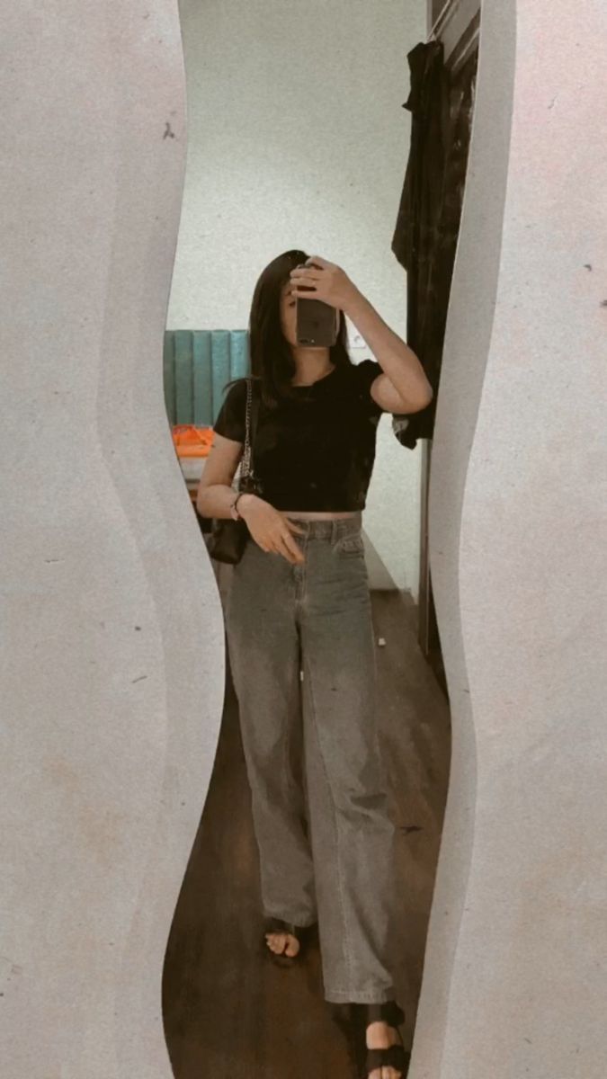 Gái trẻ mặc áo crop top đen và quần jeans rộng tạo dáng chụp ảnh trong gương