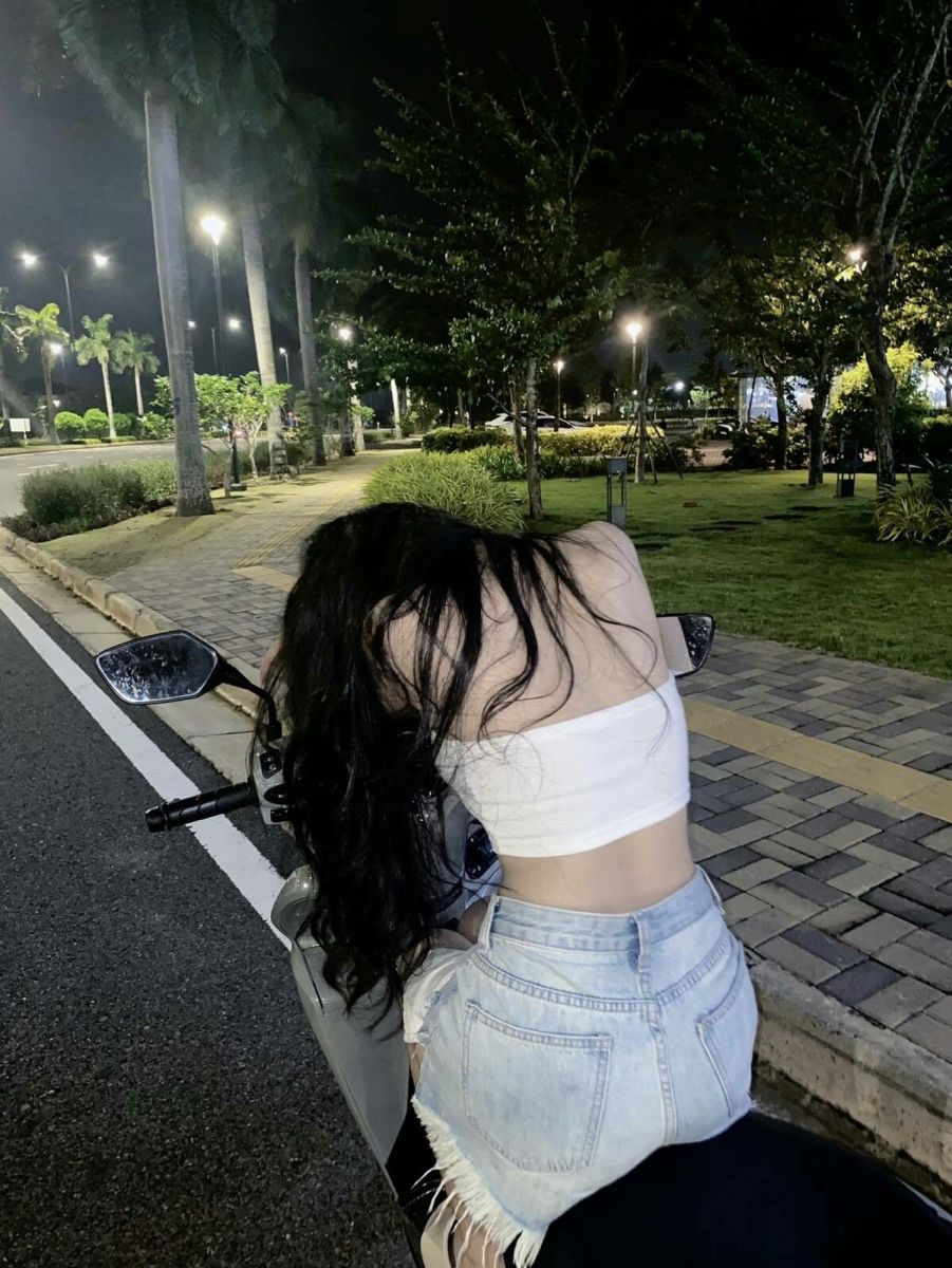 Gái trẻ mặc áo crop top trắng và chân váy jeans ngồi trên xe máy đêm tối