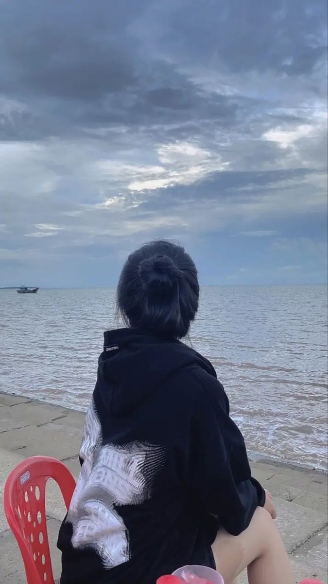 Gái trẻ trong áo hoodie đen ngồi bên bờ biển
